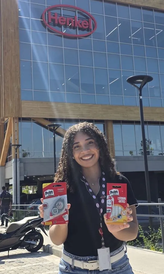 Estagiária da Henkel segurando produtos Pritt em frente ao prédio da empresa