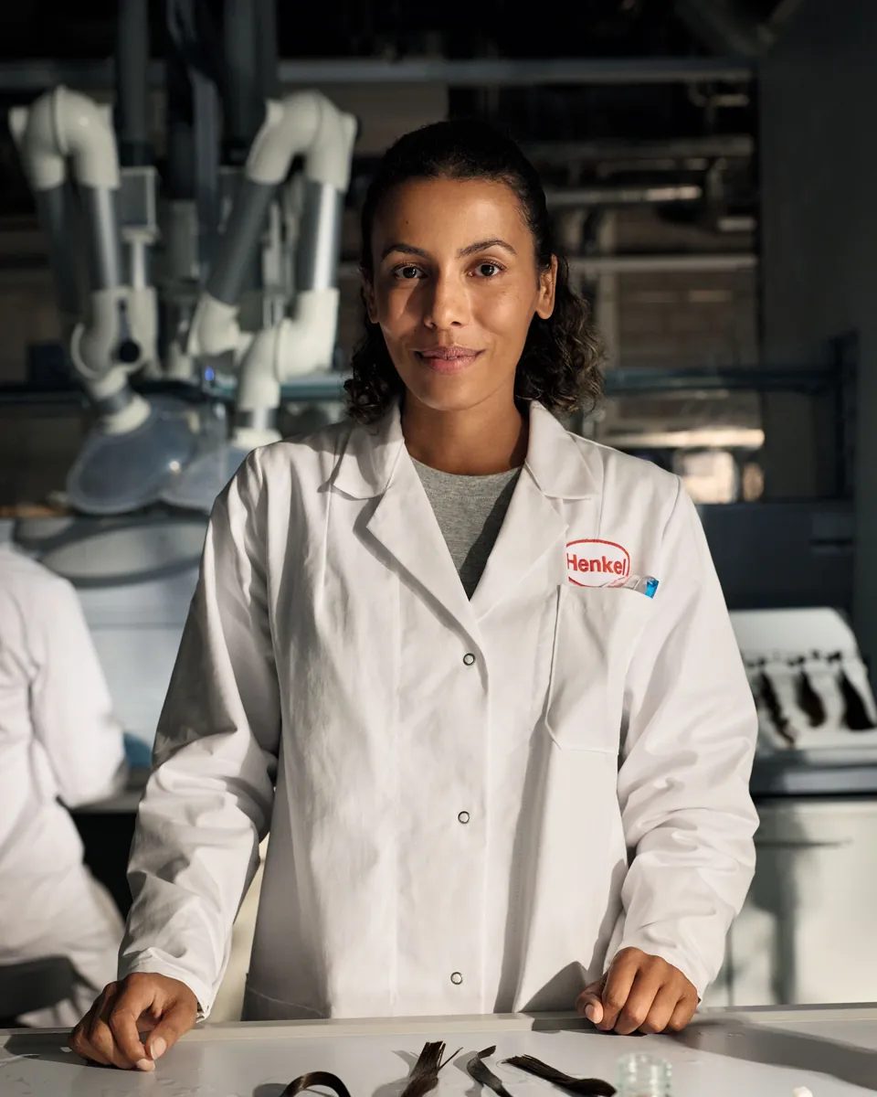 Pesquisadora de jaleco Henkel sorrindo em uma bancada de laboratório